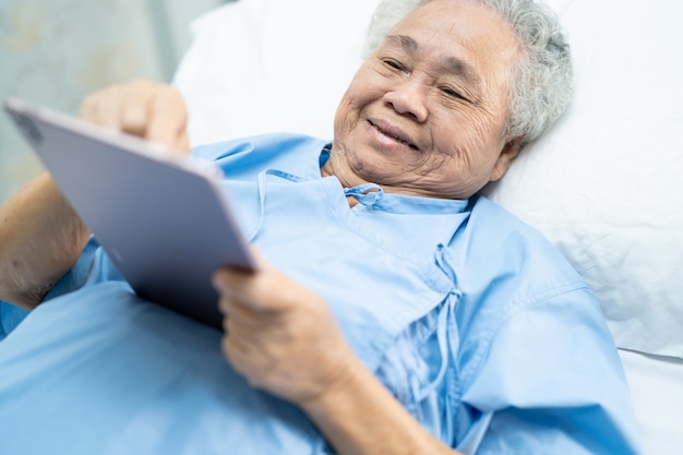 Paciente mujer mayor asiática sosteniendo en sus manos tableta digital