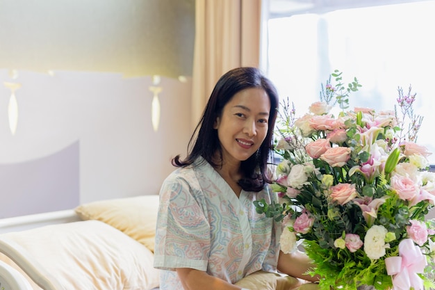 Paciente mujer sonriendo y sosteniendo un ramo de flores sentado en la cama del hospital
