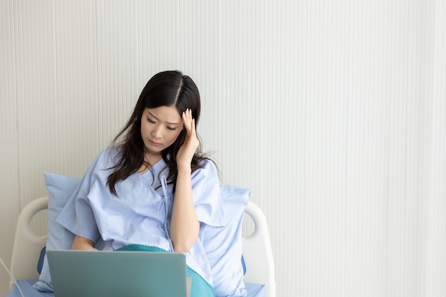 Paciente de mujeres asiáticas acostado en una cama de hospital usando una computadora portátil