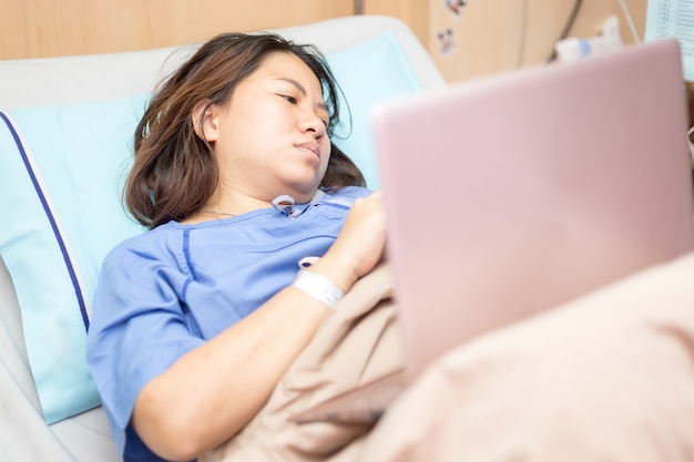 Paciente mulher asiática trabalhando com laptop durante no hospital