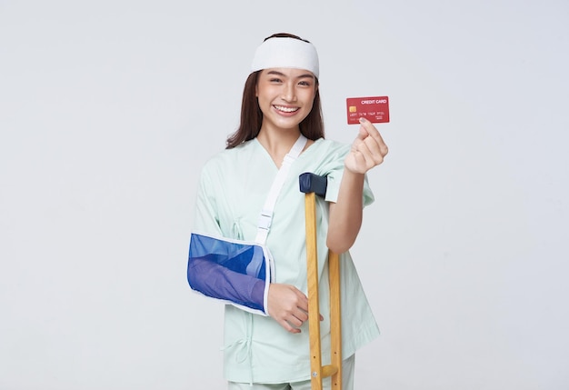 Paciente mulher colocou uma tala macia devido ao braço quebrado e entorse o pé usando muletas mostrando cartão de crédito