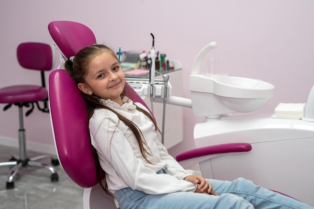 Una paciente niña muestra su aprobación para aprobar el servicio dental pediátrico en una clínica infantil moderna Centrarse en un niño positivo sonriente feliz Buen estado de la cavidad oral el niño está sentado en el sillón dental