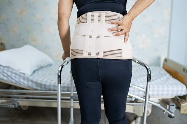 Paciente senhora asiática usando cinto de suporte de dor nas costas para lombar ortopédico com andador.