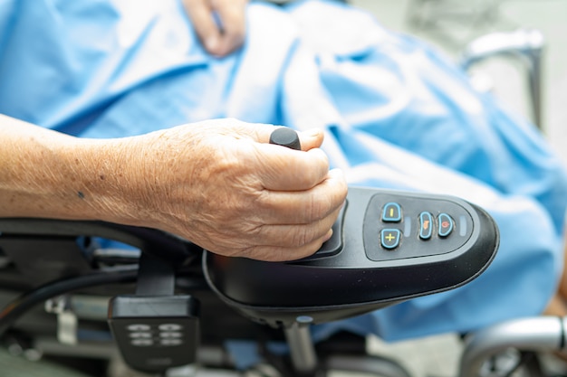 Paciente sênior asiático da mulher na cadeira de rodas elétrica com controlo a distância no hospital.