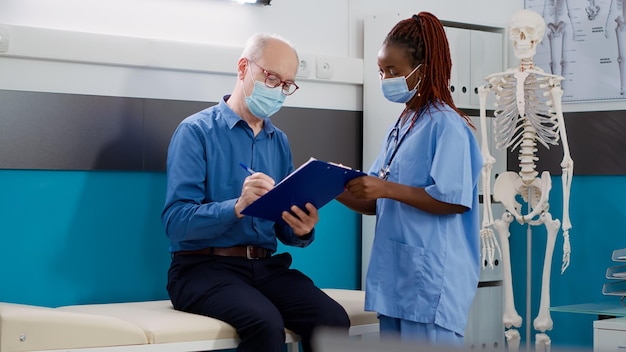 Paciente sênior assinando formulário médico no check-up com enfermeira durante pandemia de coronavírus. Velho fazendo consulta com especialista, recebendo tratamento de prescrição.