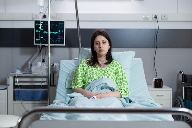 Paciente sentado erguido en la cama del hospital con aspecto de estar mal conectado para monitorear la medición de los signos vitales en la sala del hospital. Mujer con enfermedad y baja saturación de oxígeno esperando que el médico haga una consulta clínica.