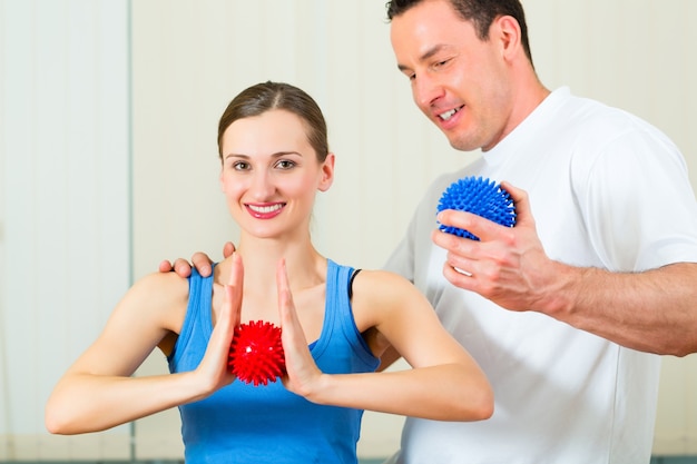 Paciente de sexo femenino en la fisioterapia haciendo ejercicios físicos con su terapeuta, utilizando una bola de masaje