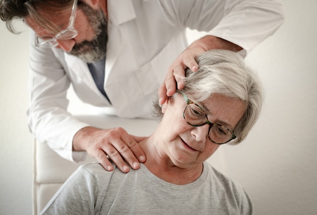 Paciente de sexo femenino mayor mientras que el tratamiento del ejercicio para el cuello con su fisioterapeuta. Dolor en las vértebras del cuello de una mujer mayor y rehabilitación en el centro médico