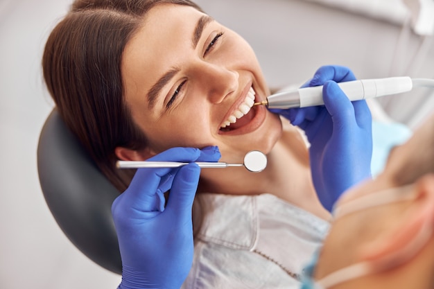 Paciente de sexo femenino en el procedimiento dental, médico con instrumentos dentales en la clínica dental moderna.