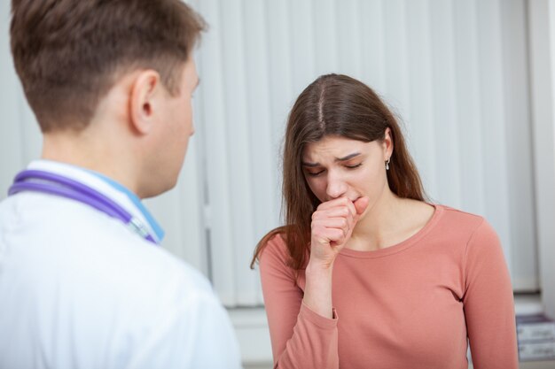 Paciente de sexo femenino que tose mientras habla con su médico