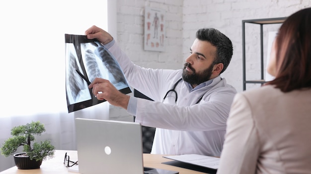 Foto paciente de sexo femenino que visita al médico de familia masculino en el consultorio médico para obtener el resultado del diagnóstico en la película de rayos x