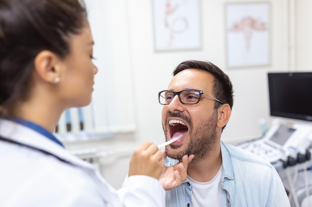 Paciente varón abriendo la boca para que el médico le mire la garganta Doctora examinando el dolor de garganta del paciente en la clínica El otorrinolaringólogo examina el dolor de garganta del paciente