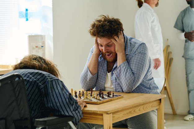 Paciente varón nervioso del hospital psiquiátrico gritando durante el juego de ajedrez