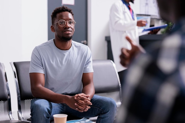 Pacientes afroamericanos hablando sobre atención médica y diagnóstico en el vestíbulo de la sala de espera del centro de salud. Grupo de hombres sentados en el área de recepción del hospital antes de asistir al examen de control.