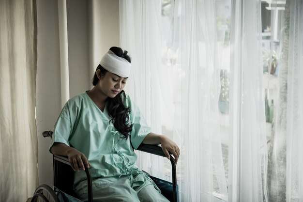 Pacientes mujeres con dolor en la cabeza después de la hospitalización sentados en silla de ruedas en la habitación del paciente