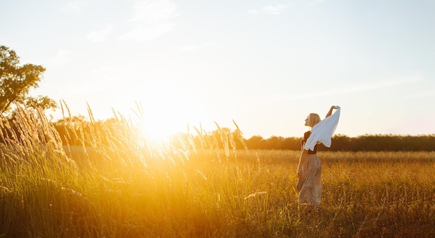 Pacífica jovem loira em pé no meio do campo de trigo contra o pôr do sol