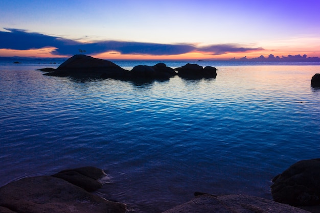 Pacífica puesta de sol azulada con siluetas de rocas sobre el mar en calma en la isla de Koh Phangan, Tailandia