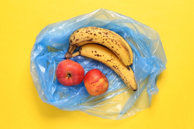 Pacote de lixo com maçãs estragadas e bananas em fundo amarelo