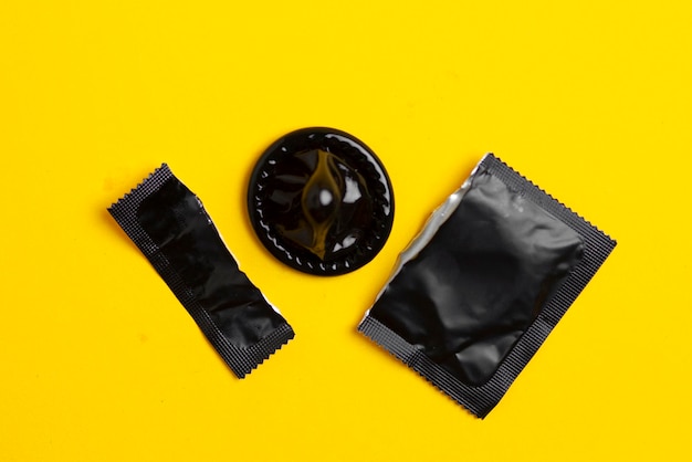 Foto pacote preto de um preservativo rasgado encontra-se em um fundo amarelo o conceito de sexo seguro