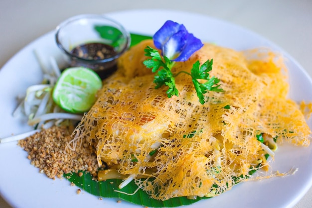 Pad Thai envuelto en huevo es una deliciosa comida tailandesa. El estilo tailandés de fideos fritos con gambas se sirve con brotes de soja frescos y limón verde en un plato blanco en el restaurante.