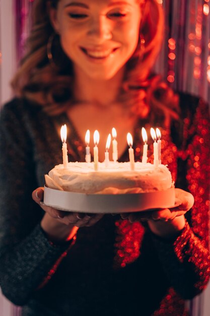 Padaria festiva Mulher feliz Celebração de aniversário Inspirada senhora sorridente se sentindo maravilhada segurando bolo com luzes de velas no fundo da cortina de cascata roxa cintilante