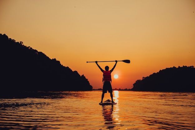 Foto paddel stehend, silhouette des mannes am strand bei sonnenuntergang