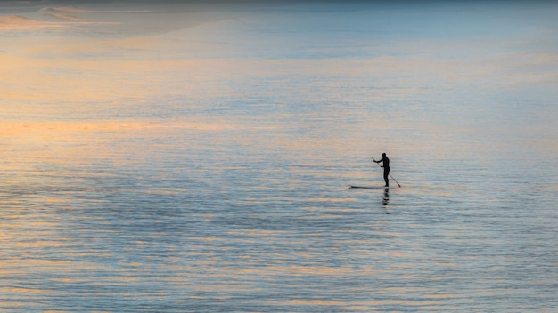 Paddle boarder en el océano remando durante la puesta de sol silueta shot realizado en christchurch, nueva zelanda