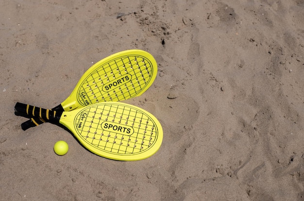 Foto paddle-tennisschläger und ball in gelber farbe am strand. kopierraum. sommersport-hintergrund