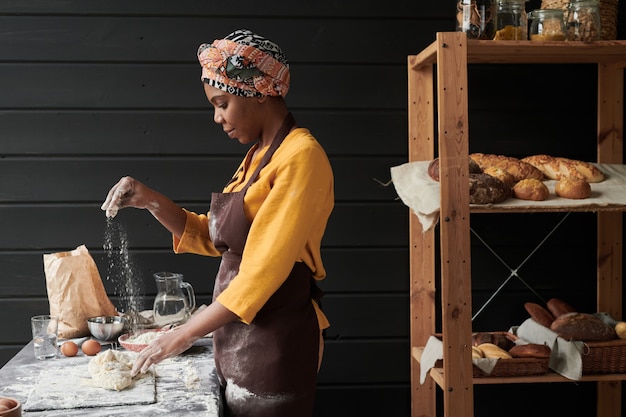 Padeiro africano de avental fazendo massa e assando pão caseiro enquanto trabalhava na padaria