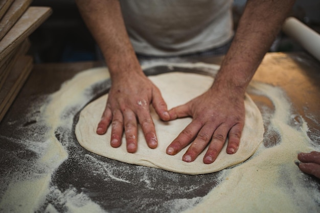 Padeiro amassando massa de pizza com as mãos na cozinha da padaria