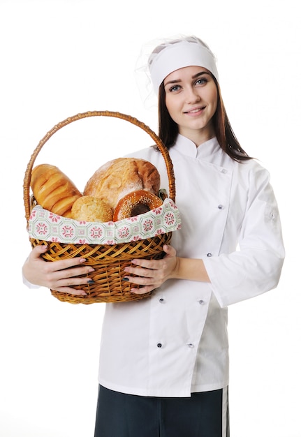 Padeiro bonito da moça no uniforme branco que guarda uma cesta com produtos da padaria em um fundo branco.