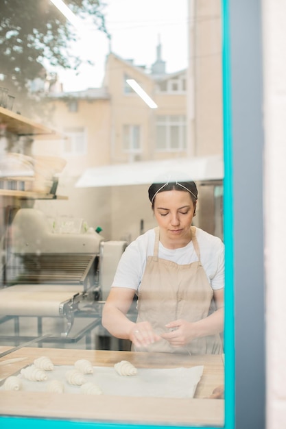 Padeiro de mulher fazendo croissants na padaria em frente à janela