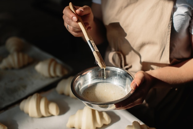 Padeiro feminino mancha croissants crus com uma escova na gema o processo de cozimento