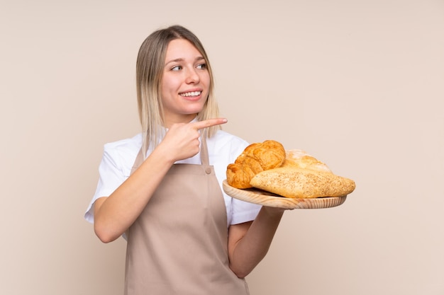 Padeiro feminino segurando uma mesa com vários pães apontando para o lado para apresentar um produto