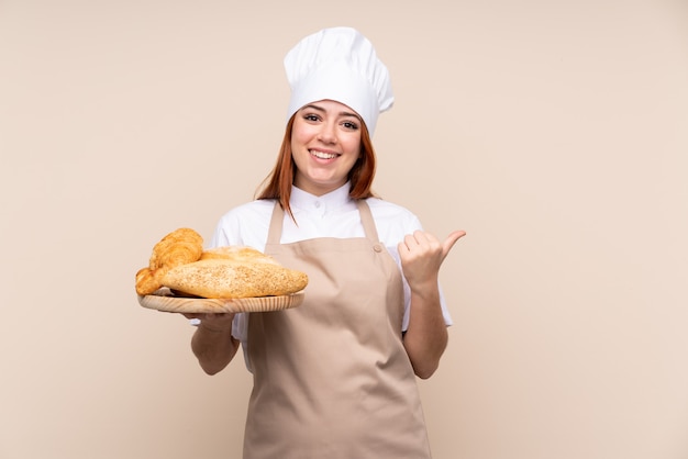 Padeiro feminino segurando uma mesa com vários pães apontando para o lado para apresentar um produto