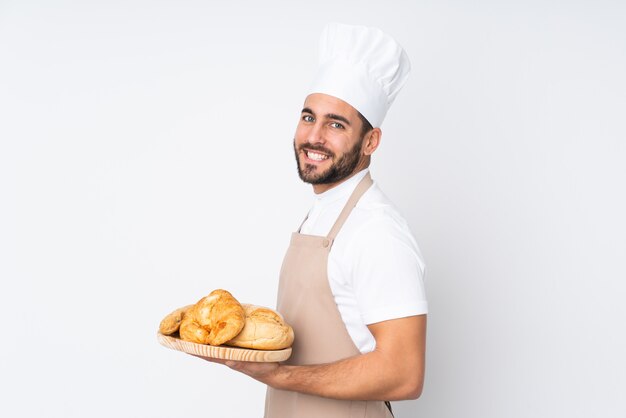 Padeiro masculino segurando uma mesa com vários pães isolados na parede branca rindo