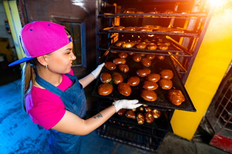Foto padeiro profissional jovem mulher bonita de uniforme bandeja de pães frescos no contexto de uma padaria ou fábrica de pão a produção de padaria