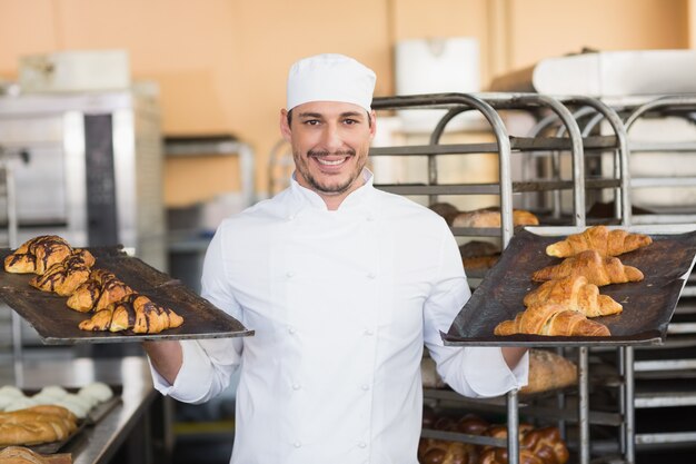 Padeiro sorridente segurando bandejas de croissants