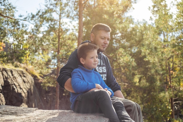 Padre abraza a su hijo disfrutando del tiempo que pasan juntos entre padre e hijo niño feliz sonriendo con dientes Bosque de otoño Padre hijo Familia feliz al aire libre