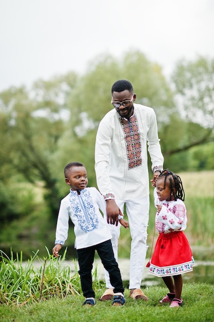 Padre africano con niños vestidos con ropa tradicional en el parque.