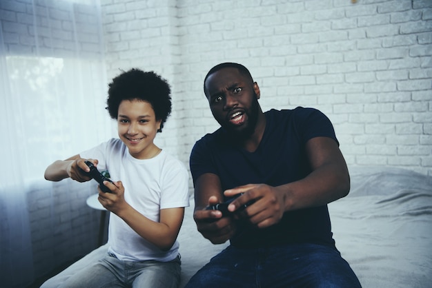 Padre afroamericano con hijo juega videojuegos.