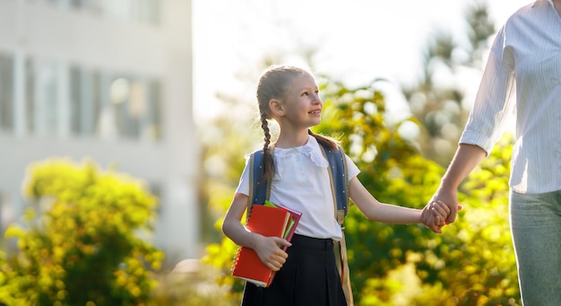 Padre y alumno de escuela primaria yendo de la mano Mujer y niña con mochila