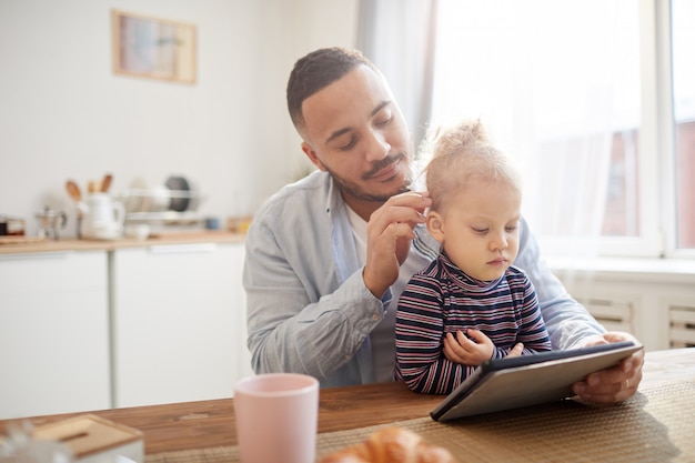 Padre amoroso con tableta digital con niña linda