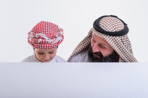 Padre árabe con hijo sosteniendo cartel blanco y sacando la lengua foto de stock