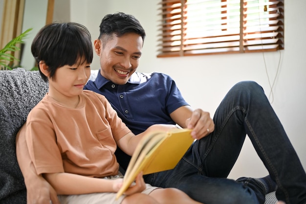 Un padre asiático alegre disfruta leyendo un libro o contándole una historia a su pequeño hijo