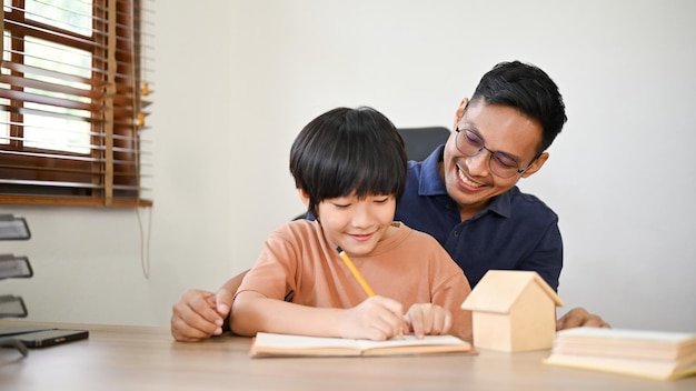 Un padre asiático cariñoso enseñando a su hijo a escribir el alfabeto en un papel