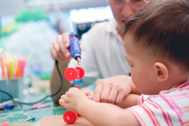 Padre asiático enseñando a niños a hacer juguetes para automóviles con materiales reciclados.