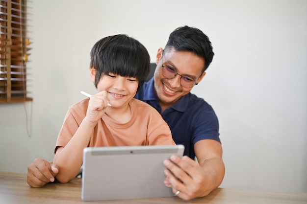 Un padre asiático feliz disfruta viendo el contenido de video de un niño en una tableta con su hijo