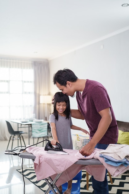 Padre asiático con hija pequeña planchando ropa en casa