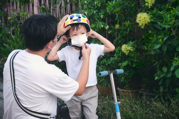 Padre asiático pasar tiempo con su pequeño hijo montando scooter en la ciudad